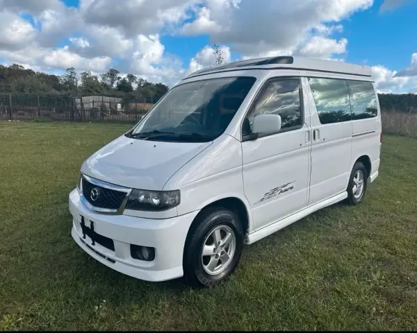 Biały van Mazda Bongo z podnoszonym dachem, zaparkowany na trawie.