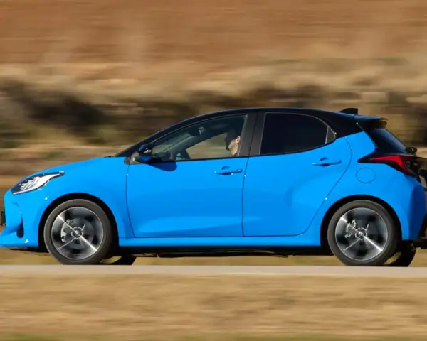 Niebieski hatchback z czarnym dachem pędzi po drodze, za kierownicą siedzi mężczyzna.
