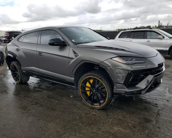 Szary Lamborghini Urus z żółtymi akcentami na felgach, uszkodzony z przodu. Zastanawiasz się nad lamborghini urus cena?