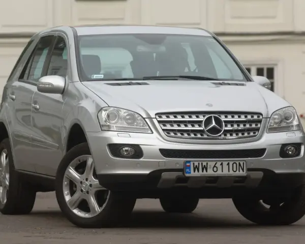 Srebrny Mercedes ML 320 z polskimi tablicami rejestracyjnymi WW 6110N zaparkowany przed budynkiem.