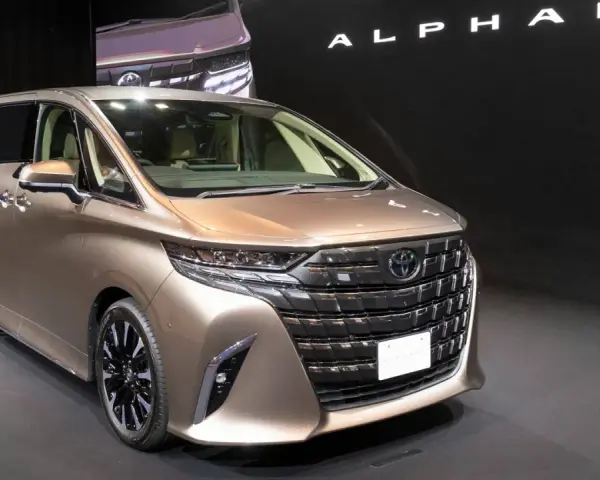 Brązowy minivan Toyota Alphard na ciemnym tle, z widocznym napisem "ALPHARD".