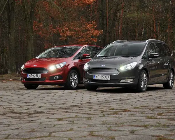 Dwa samochody Ford, czerwony S-Max i szary Galaxy, stoją na brukowanej nawierzchni w jesiennym lesie.