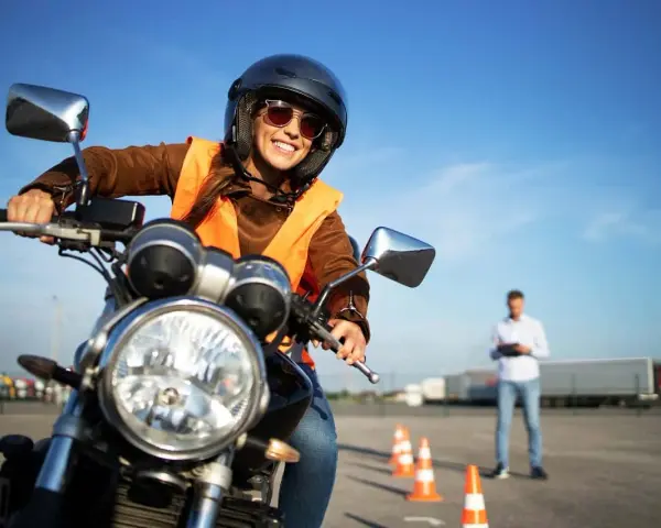 Uśmiechnięta kursantka na motocyklu, gotowa do egzaminu na prawo jazdy kat. A. Sprawdza cenę kursu.