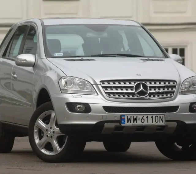 Srebrny Mercedes ML 320 z polskimi tablicami rejestracyjnymi WW 6110N zaparkowany przed budynkiem.