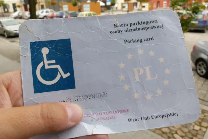 Karta parkingowa dla niepełnosprawnych, z symbolem wózka inwalidzkiego i gwiazdkami UE. Ułatwia parkowanie w mieście.