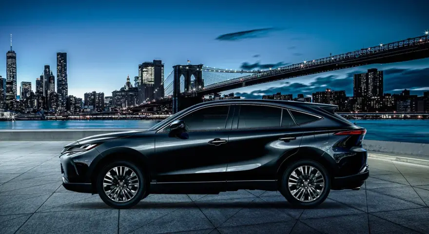 Elegancki, czarny Toyota Harrier lśni nocą na tle rozświetlonego miasta i mostu.
