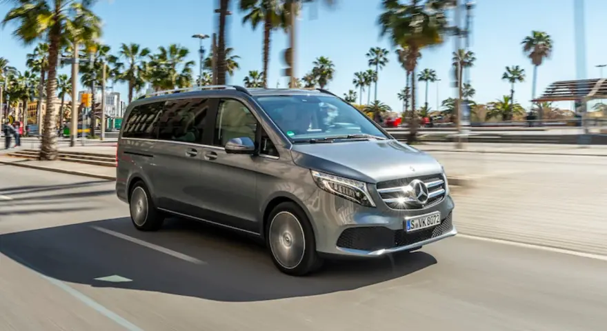 Szary Mercedes minivan jedzie ulicą w słoneczny dzień, otoczony palmami.