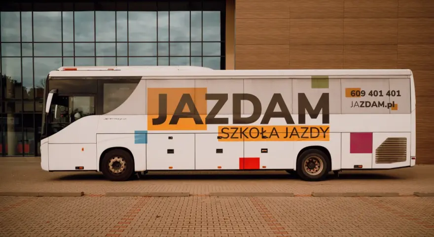 Biały autobus szkolny z napisem "JAZDAM SZKOŁA JAZDY" i numerem telefonu.