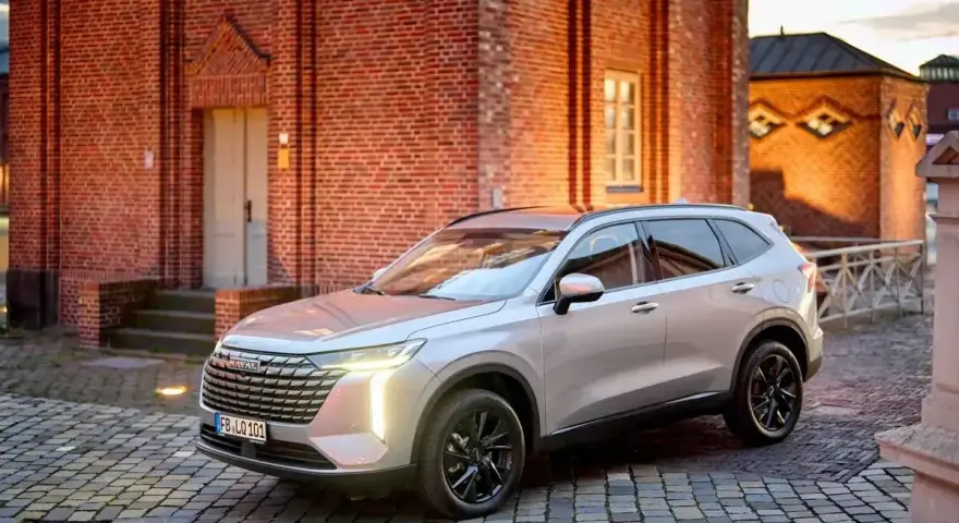 Srebrny Haval SUV zaparkowany na brukowanym dziedzińcu przed ceglanym budynkiem.