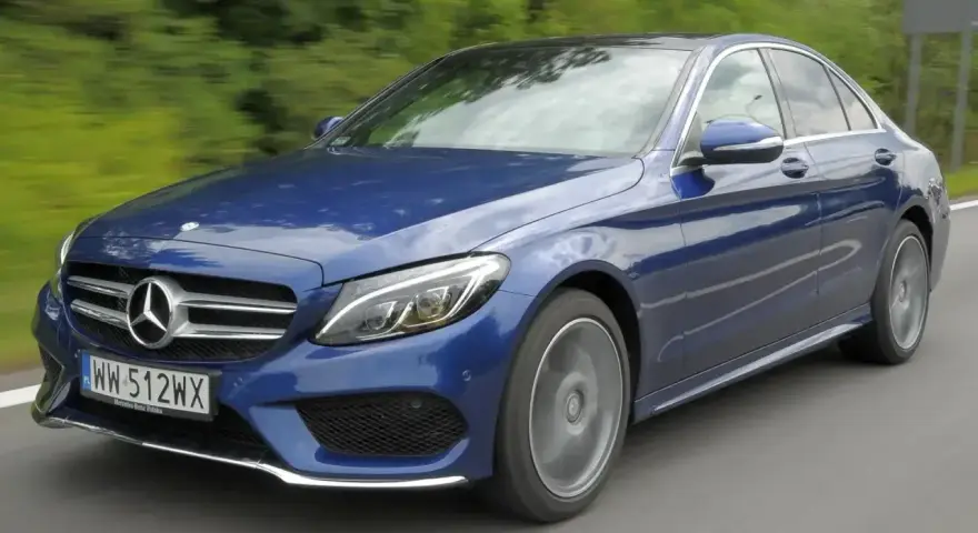 Błękitny Mercedes E220d w ruchu, z rozmytym tłem zieleni i drogi. Elegancki sedan na polskich tablicach rejestracyjnych.