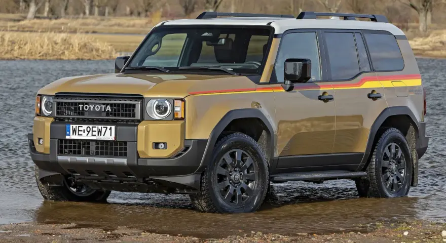 Złoty Toyota Land Cruiser Prado z kolorowymi pasami na boku, wjeżdża do wody.