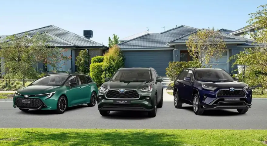 Trzy modele Toyota SUV: zielony kombi, ciemnozielony Highlander Hybrid i granatowy RAV4 Plug-in Hybrid, zaparkowane przed domami.