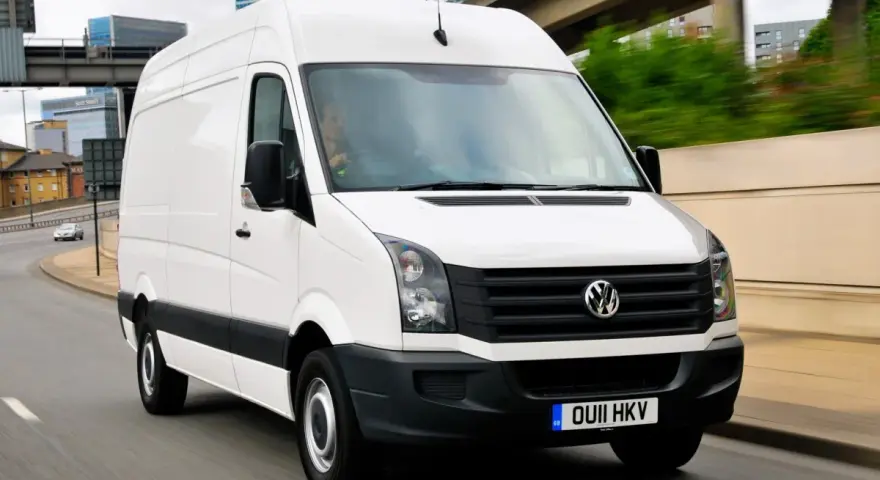Biały Volkswagen Crafter 2.5 TDI w ruchu miejskim, z widocznymi budynkami w tle.