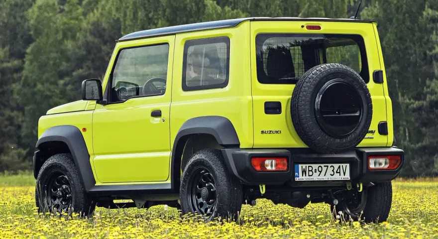 Jaskrawożółty Suzuki Jimny na tle łąki z żółtymi kwiatami. Sprawdź aktualną suzuki jimny cena i wybierz się na przygodę!