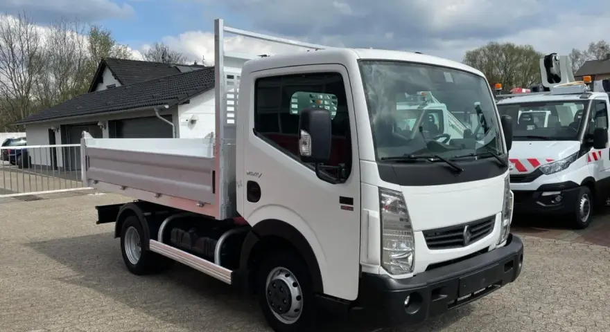 Biały Renault Maxity z otwartą skrzynią ładunkową stoi na placu. W tle budynek i inne pojazdy.
