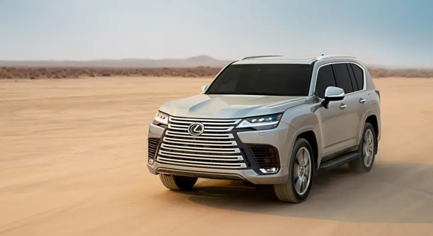 Srebrny Lexus LX 600 przemierza pustynię, zostawiając ślady na piasku.