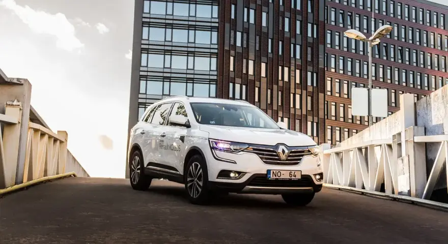Biały Renault Koleos na tle nowoczesnego budynku. Czy warto zainwestować? Sprawdź interrisk opinie.