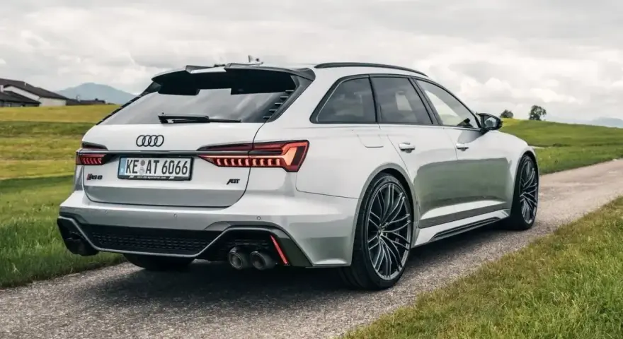 Srebrne Audi RS6 Avant z pakietem ABT na tle zielonych wzgórz. Sprawdź audi rs6 cena i możliwości tego potwora.