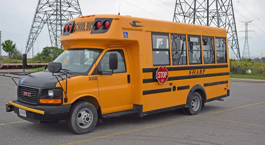 Żółty autobus szkolny GMC z napisem "SHARP" i znakiem STOP. Zastanawiasz się, ile kosztuje autobus?