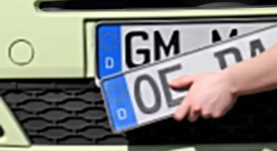 Dłoń trzyma niemieckie tablice rejestracyjne z literami "OE" i "GM".