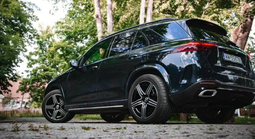 Ciemny Mercedes GLE 350 zaparkowany na kamienistej drodze, otoczony zielenią drzew.