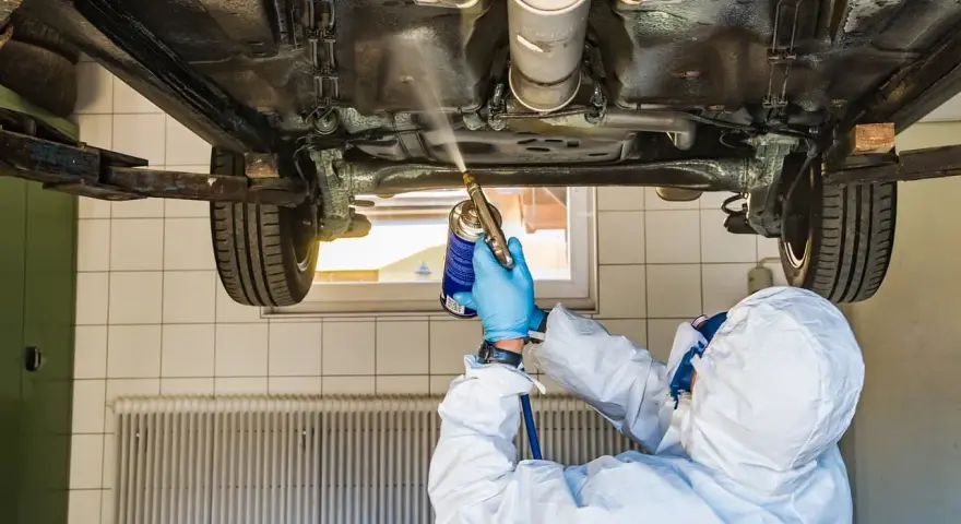 Mechanik w kombinezonie zabezpieczającym podwozie samochodu. Zastanawiasz się, ile kosztuje przegląd samochodu z gazem?