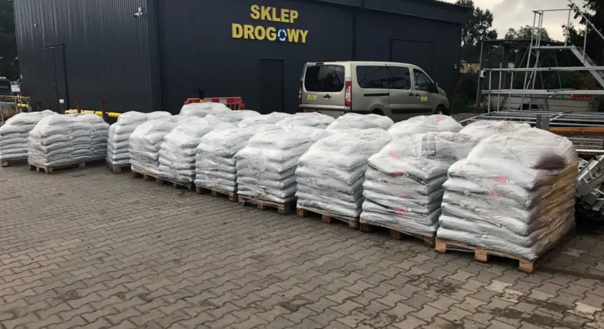 Palety z workami materiałów budowlanych przed sklepem drogowym.