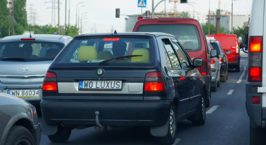Czarny samochód z indywidualnymi tablicami rejestracyjnymi "WO LUXUS" w korku ulicznym.