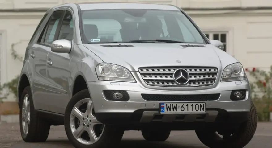 Srebrny Mercedes ML 320 z polskimi tablicami rejestracyjnymi WW 6110N zaparkowany przed budynkiem.