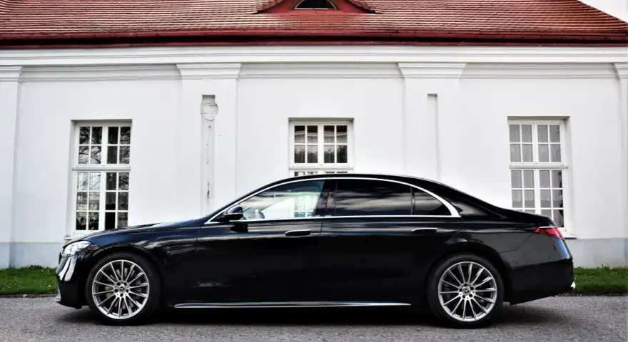 Elegancki, czarny Mercedes S500 lśni na tle białej, zabytkowej fasady z czerwonym dachem.