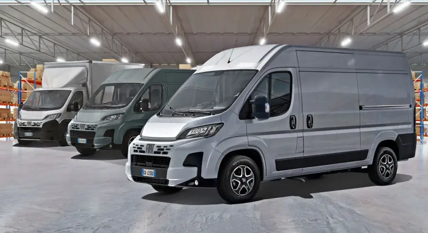 Rząd szarych furgonetek Fiat Ducato Maxi w magazynie z półkami i pudełkami.