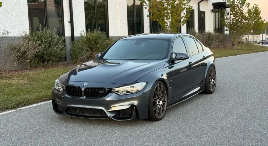 Szary sedan BMW M3 na tle nowoczesnego budynku. Sprawdź aktualną bmw m3 cena i możliwości tego sportowego auta.