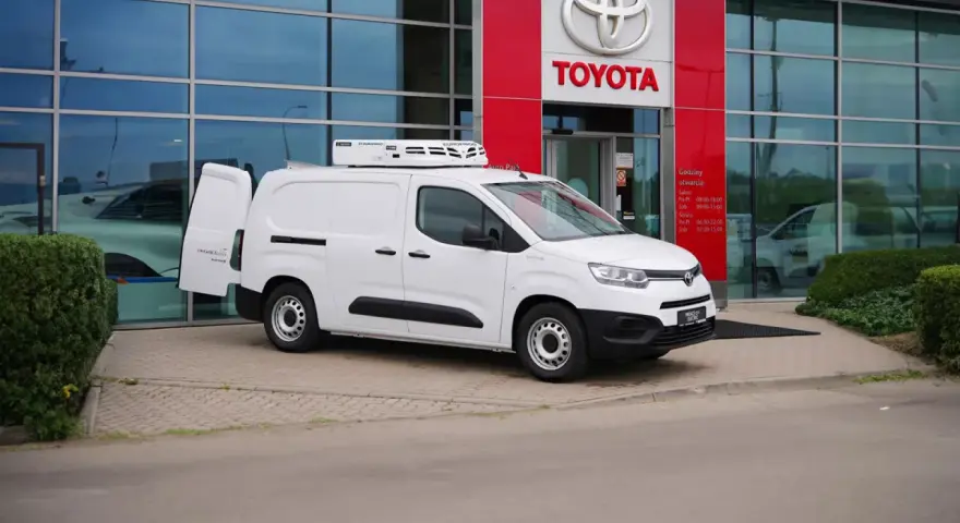 Biały, mały dostawczak z chłodnią na dachu stoi przed salonem Toyoty.