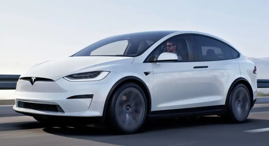 Biała Tesla Model X w ruchu. Zastanawiasz się, ile kosztuje Tesla? Ten luksusowy SUV elektryczny to marzenie wielu kierowców.
