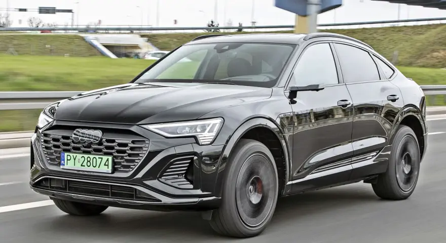Czarny Audi Q8 e-tron sunie po drodze. Zastanawiasz się nad audi q8 cena? Ten luksusowy SUV coupe robi wrażenie.