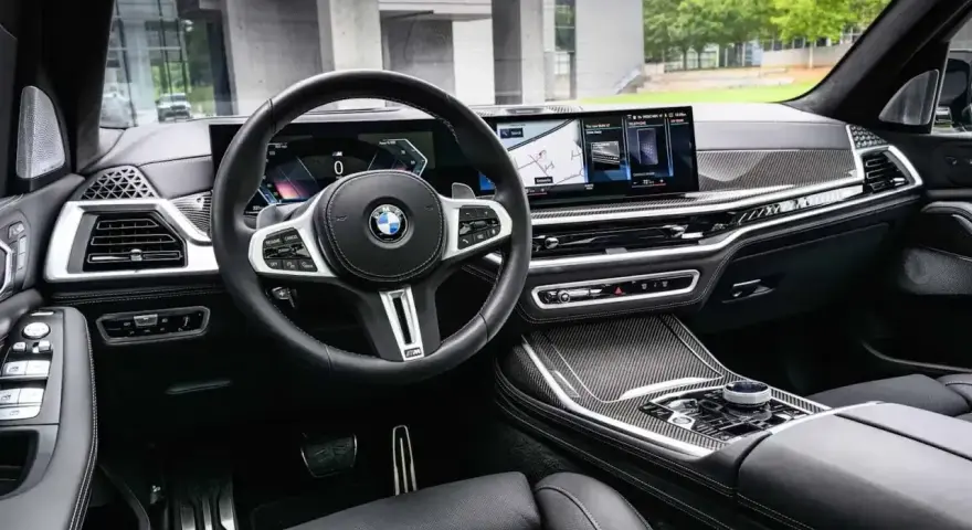 Wnętrze BMW x7: skórzana tapicerka, nowoczesny kokpit z dwoma ekranami i sportowa kierownica.