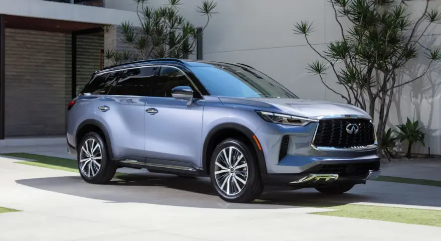 Elegancki, srebrny Infiniti SUV zaparkowany przed nowoczesnym domem z bujną roślinnością.
