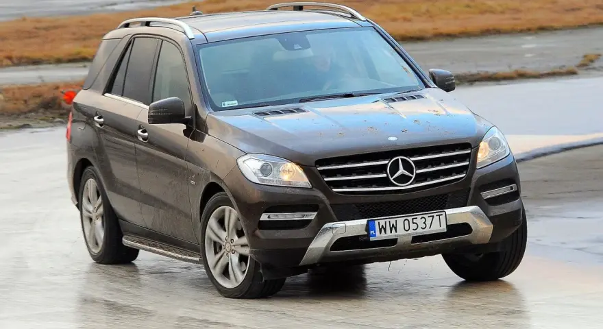 Brązowy Mercedes-Benz ML na mokrej nawierzchni, z widoczną tablicą rejestracyjną WW 0537T.
