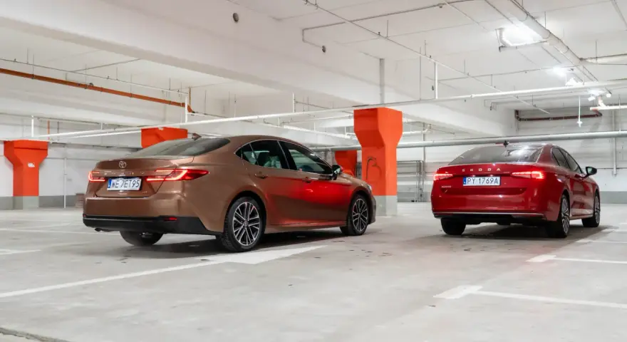 Brązowa Toyota Camry i czerwona Skoda Superb stoją w garażu podziemnym.