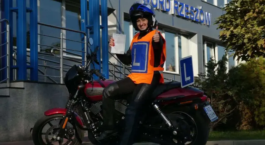 Szczęśliwa kursantka z prawem jazdy kat. A na motocyklu, w kamizelce z literą L, przed budynkiem WORD.