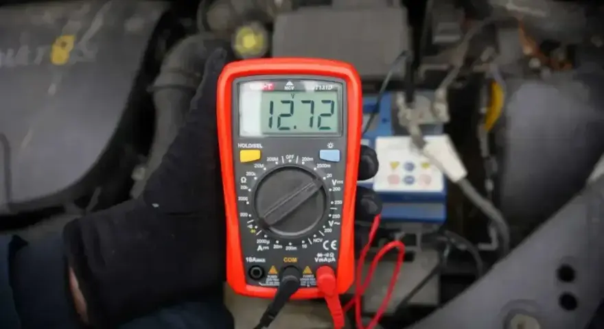 Multimetr pokazuje 12.72V, co oznacza prawidłowe napięcie akumulatora. Sprawdzanie stanu baterii przed podróżą.