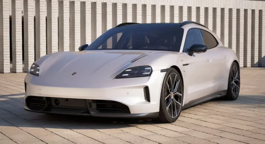 Elegancki Porsche Taycan w kolorze jasnoszarym, zaparkowany przed nowoczesnym budynkiem. Sprawdź porsche taycan cena!
