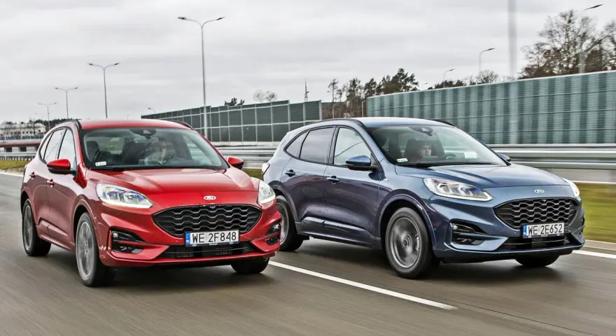Dwa Fordy SUV, czerwony i granatowy, jadące obok siebie po drodze.