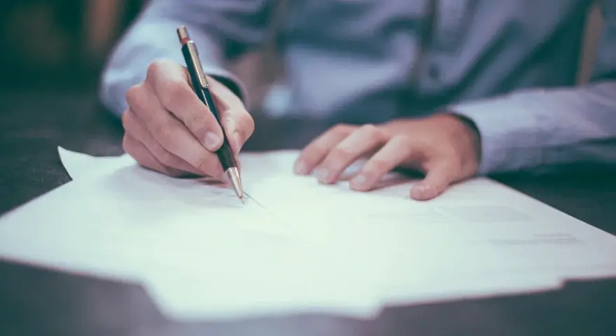 Dłoń pisze piórem na dokumencie. Może to być trasti wypowiedzenie OC lub inny ważny papier.