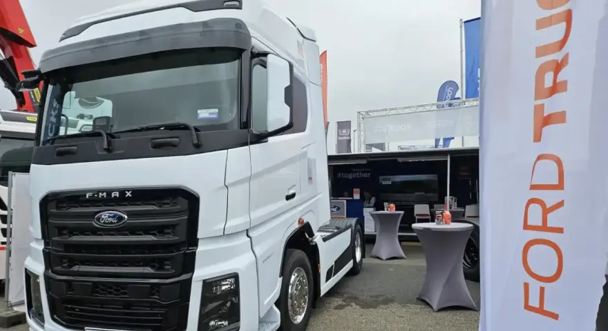 Biały Ford F-MAX prezentuje się na wystawie, obok banerów z logo Ford Trucks.