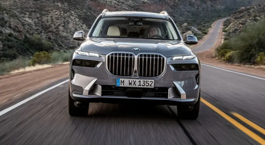 Szary BMW X7M pędzi krętą drogą przez pustynny krajobraz.