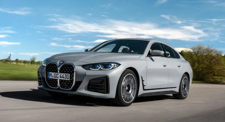 Eleganckie, szare BMW Gran Coupé sunie po drodze na tle błękitnego nieba z chmurami.