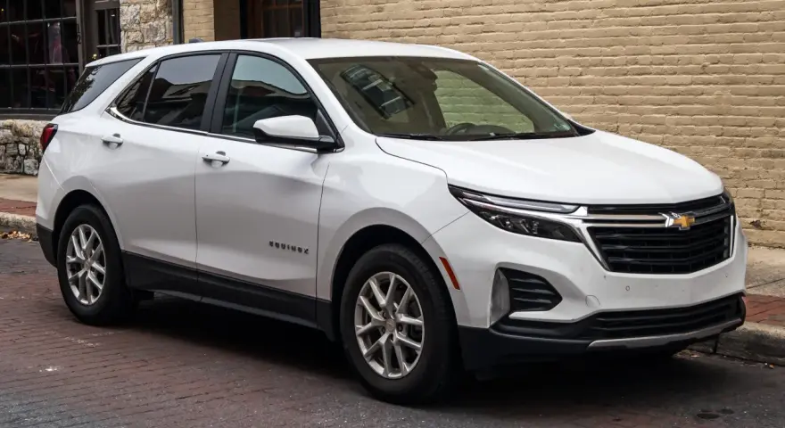 Biały Chevrolet Equinox, wszechstronny chevrolet suv, zaparkowany na brukowanej ulicy przed ceglanym budynkiem.