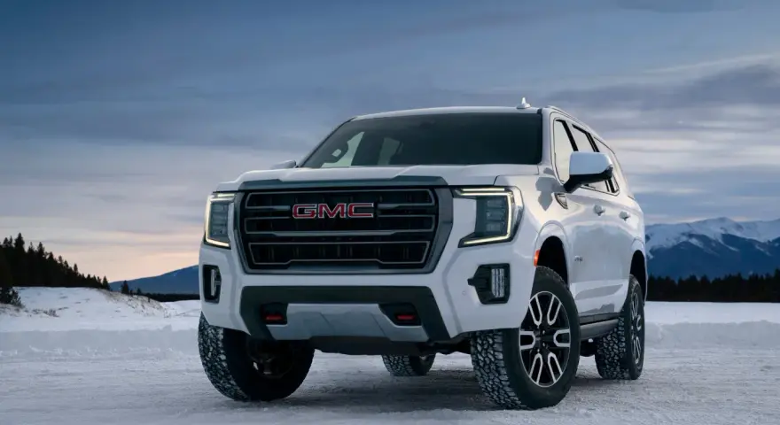 Biały GMC Yukon XL gotowy na zimową przygodę na ośnieżonej drodze, z górami w tle.