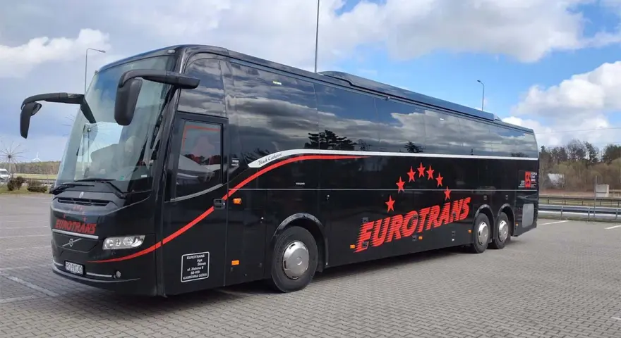 Czarny autokar turystyczny Eurotrans z czerwonymi gwiazdami i napisem na tle błękitnego nieba.